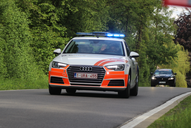 Ein Polizei-Audi A4 fährt auf einer grasbewachsenen Straße neben einem Wald, mit zwei Personen darin, unter einem klaren blauen Himmel.