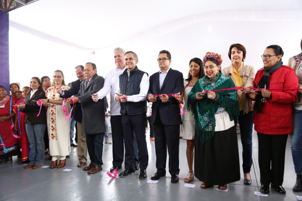 Eine Gruppe von Menschen, die mit einer Schere lächeln und eine Schnur durchschneiden, vor einer Menge mit einer Säule links und Papieren auf dem Boden.