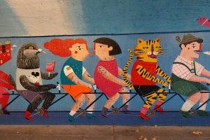 Ein Wandgemälde auf einem Gebäude in London, das Menschen beim Radfahren zeigt, mit einer Straße und einem Himmel im Hintergrund.