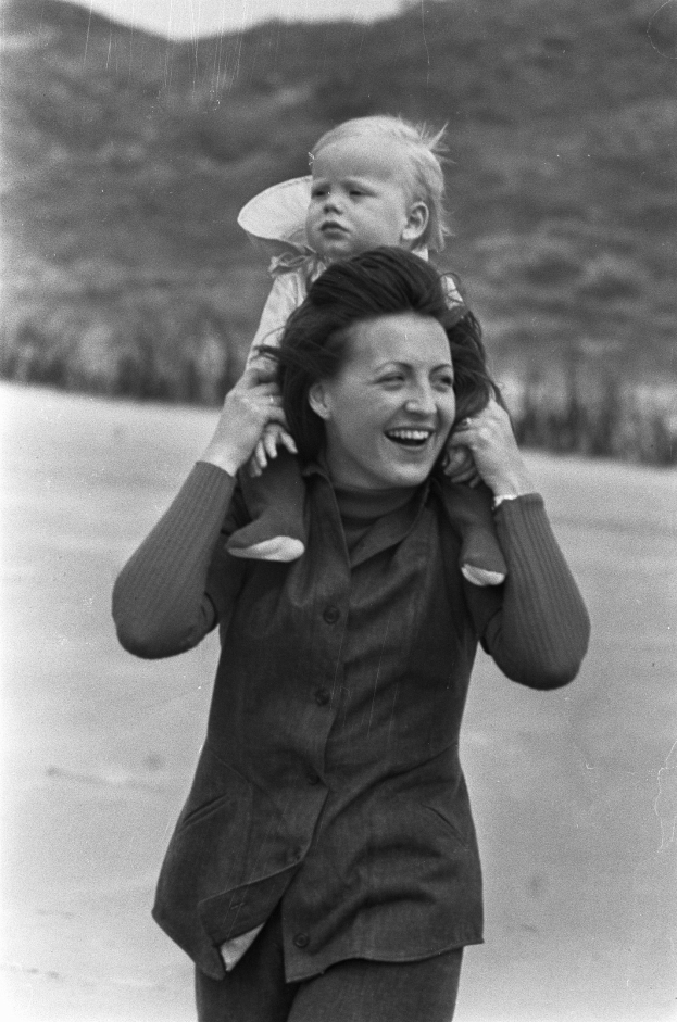 Eine Frau, die strahlend lächelt, während sie ein Baby hält, mit einem sanft unscharfen Hintergrund, der eine träumerische Stimmung schafft.