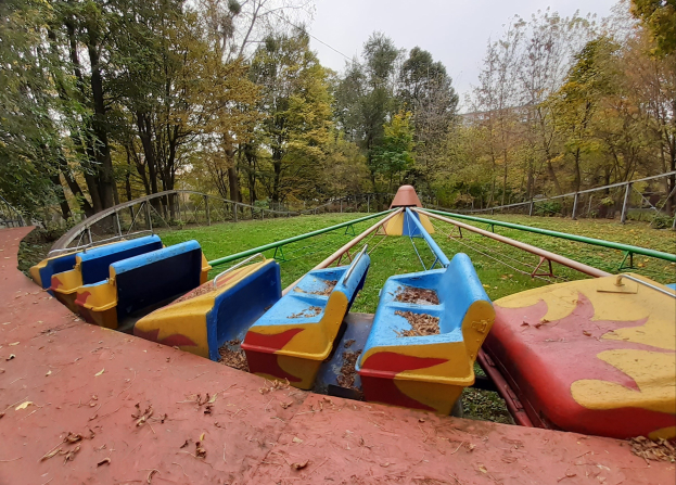 Verlassener Vergnügungspark Mit Einer Achterbahn Mit Umgebender Reling, Umgeben Von Bäumen, Gras Und Blättern, Unter Einem Sichtbaren Himmel.