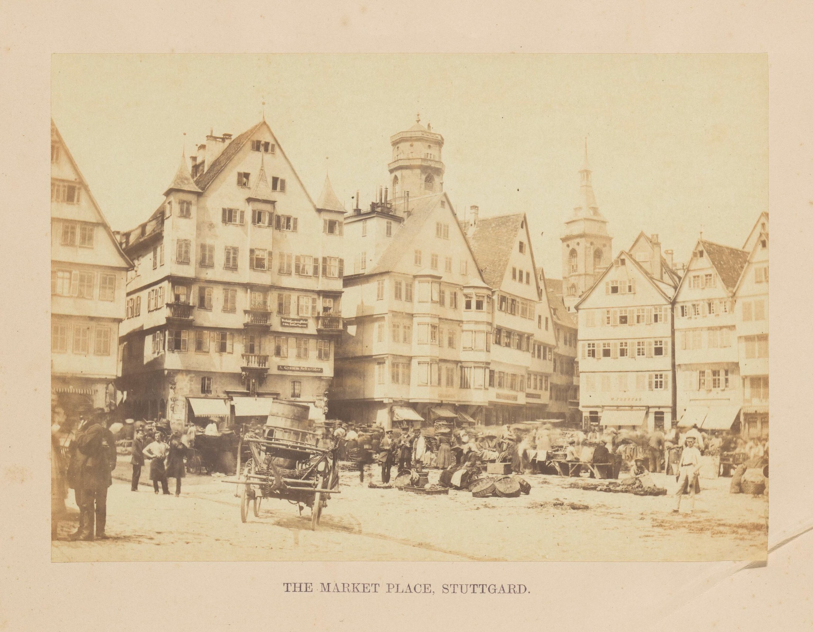 Black-and-white photo of a busy market square in Stuttgart, Germany, with buildings, people, carts, and scattered objects; text visible at the bottom.