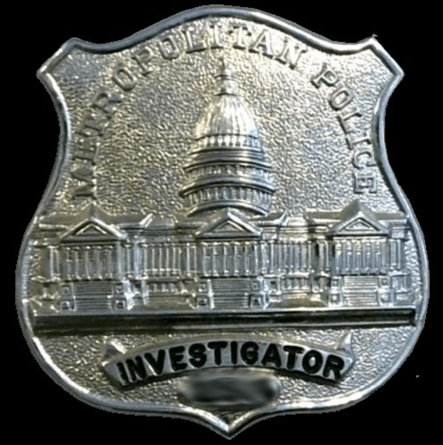 Ein silbern Polizeiabzeichen mit der Aufschrift "Ermittler" auf einem weißen Hintergrund.