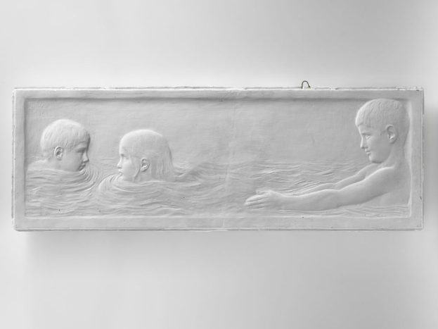 Drei Kinder schwimmen im Wasser mit einer Wand im Hintergrund.