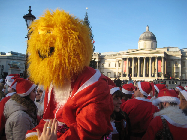 Eine Person in einem Santa-Kostüm mit einer Tiger-Maske steht mit anderen in Santa-Kostümen vor einem Gebäude.