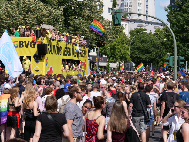 Eine große Menschenmenge, viele mit Mützen und Fahnen bekleidet, geht eine Straße in Berlin, Deutschland, entlang, mit einem gelben Lastwagen und Gebäuden im Hintergrund.
