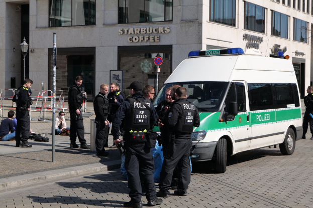 Gruppe von Polizisten vor einem Starbucks-Café mit einem Van auf der rechten Seite und Menschen auf der linken Seite, Hintergrund enthält ein Gebäude mit Fenstern, ein Schild, einen Laternenmast und eine Absperrung.