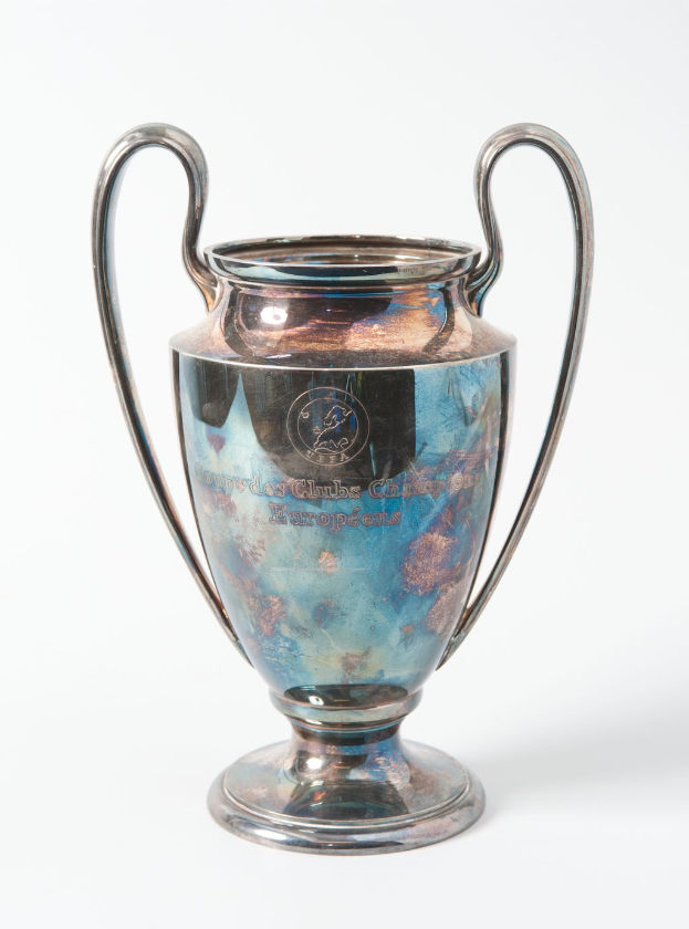 Der UEFA Champions League Pokal, ein silberner und blauer Stahlbecher mit zwei Griffen, der mit 'UEFA Champions League' beschriftet ist, vor einem weißen Hintergrund.
