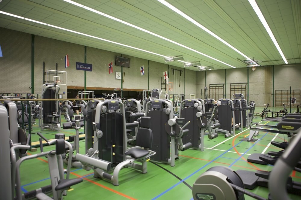 Großes Fitnessstudio mit verschiedenen Trainingsgeräten und einer Wand mit Flaggen und Deckenbeleuchtung.