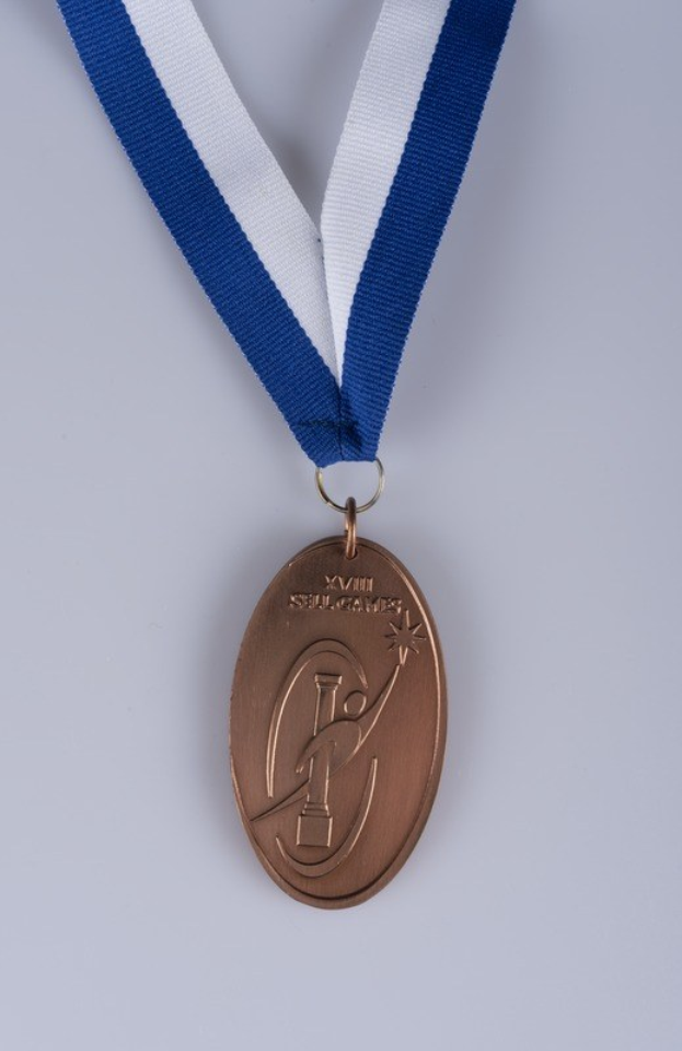 Goldene Medaille mit blau-weißem Band, eingravierter Text, auf weißem Hintergrund.
