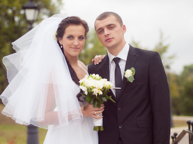 Ein Mann und eine Frau in Hochzeitskleidung stehen zusammen, die Frau hält Blumen in ihren Händen.
