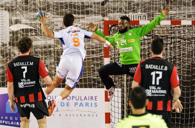 Eine Gruppe von Männern, die Handball spielen, mit einem, der springt und den Ball hält, vor einem Tor und einer Fahne mit der Aufschrift "Ligue 1 - Bordeaux vs Marseille."