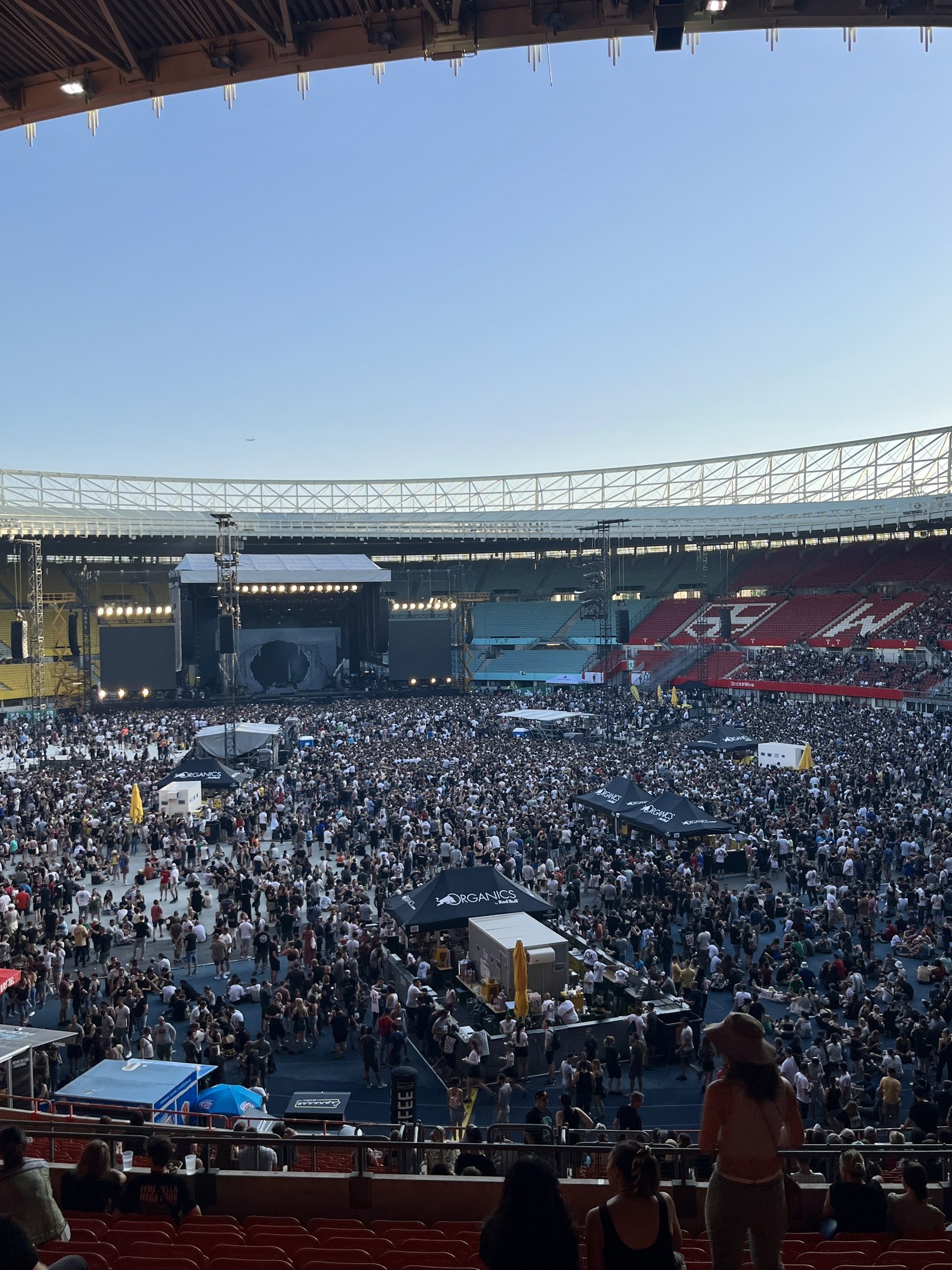 Große Menschenmenge auf Sitzplätzen und Stehplätzen in einem Stadion mit Zelten, Geländern und Überdachung während eines Events in der O2 Arena in London.