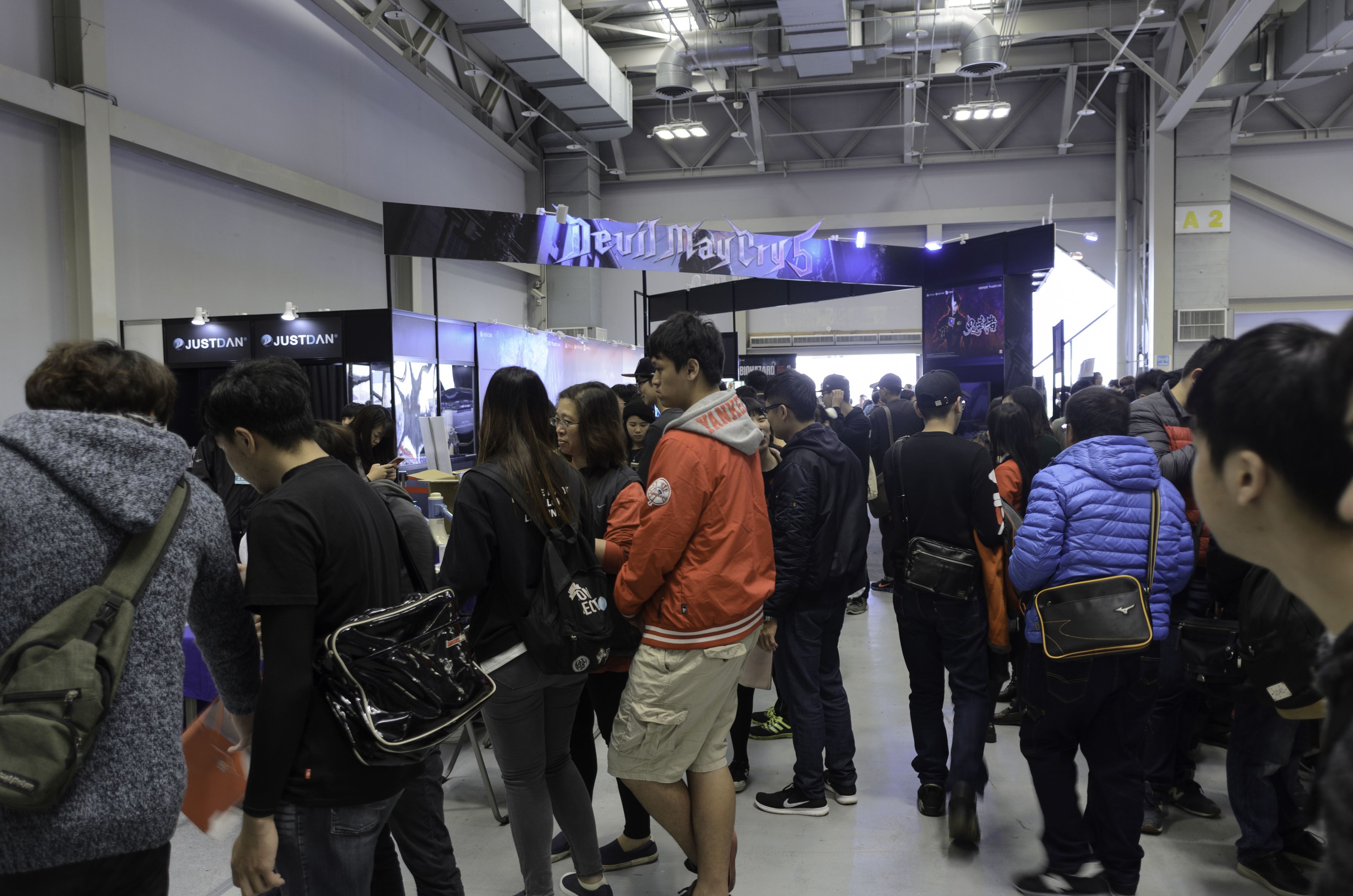 Menschen vor einer Menschenmenge auf einer Gaming-Messe, mit Texttafeln, Deckenbeleuchtung und Rohren im Hintergrund.