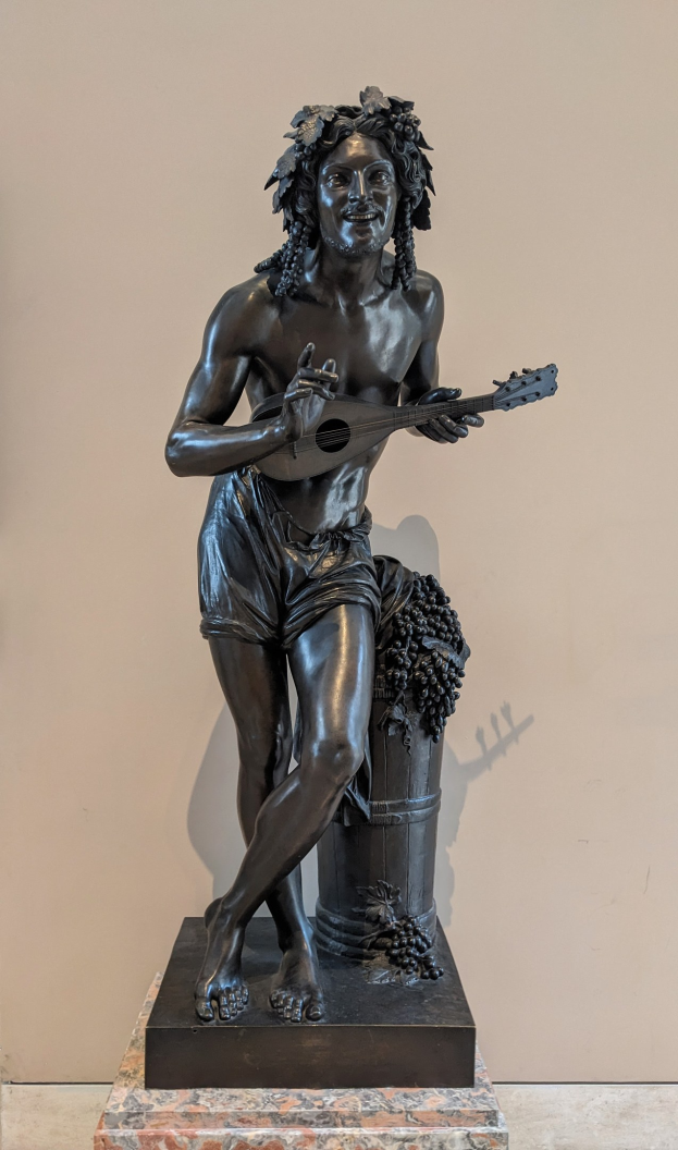 Bronzestatue eines Mannes, der eine Gitarre spielt, mit einer Wand im Hintergrund und einem Boden unten.