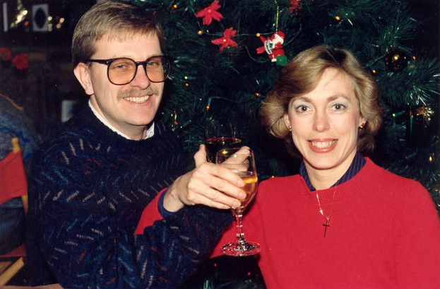 Ein Paar lächelt mit Gläsern Wein in der Hand, im Hintergrund ein Weihnachtsbaum.