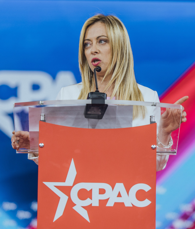 Frau in weißem Kleid, die an einem Rednerpult mit einem Mikrofon steht und als Politologin spricht.