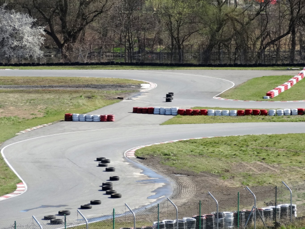 Rennstrecke mit zahlreichen Reifen entlang ihrer Kanten, gesäumt von Gras und Maschendrahtzaun, mit Bäumen im Hintergrund.