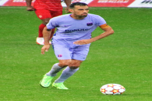 Ein Fußballer in Sportkleidung und -schuhen ist im Einsatz auf dem Feld, im Hintergrund ist eine Tafel mit Text zu sehen.