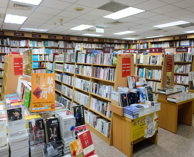 Ein gut organisierter Buchladen mit ordentlich aufgestellten Büchern auf Regalen und Tischen, mit informativen Schildern auf dem Boden und Deckenbeleuchtung.