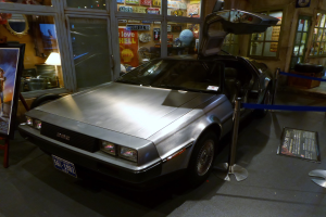 Ein DeLorean DMC-12 aus der Zurück in die Zukunft-Reihe im Museum ausgestellt, umgeben von Informationsanzeigen, Bändern und verschiedenen Gegenständen.