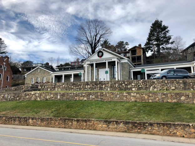Steinwand mit geparkten Autos, benachbarte Gebäude mit Fenstern und Türen, Bäume und ein bewölkter Himmel im Hintergrund, als das kürzlich wiedereröffnete Weltkulturerbe-Museum bezeichnet.