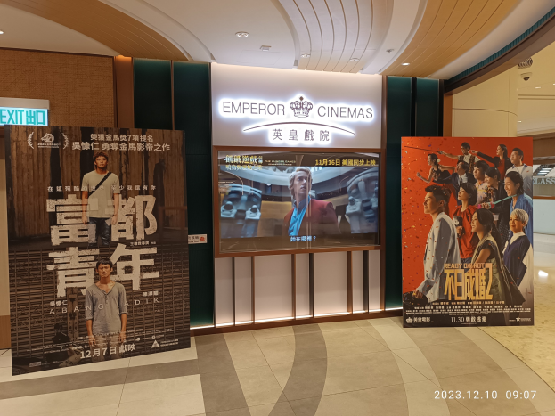 Eintritt zum Emperor Cinemas in Hong Kong mit Bannern, einem Bildschirm, einer Namensschild, Deckenleuchten und einem Wasserzeichen.