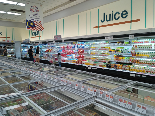 Ein gut beleuchteter Supermarktwörter mit Flaschengetränken, frischem Obst und anderen Lebensmitteln, sowie einigen Einkaufenden und Deckenbeleuchtung.