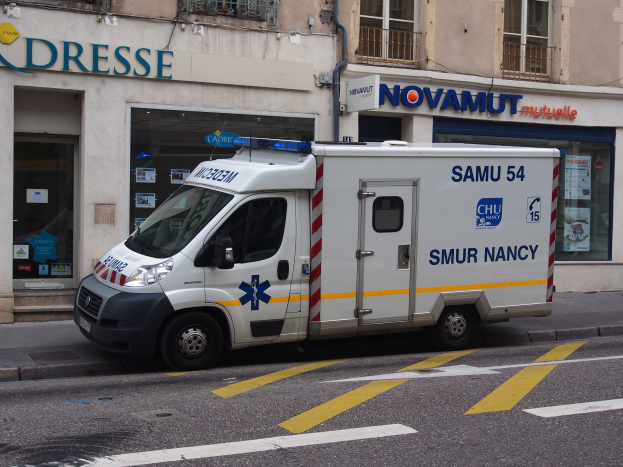 Ambulanz auf dem Seitenstreifen vor einem Krankenhausgebäude mit Fenstern, Geländern, Schildern, Plakaten und anderen Gegenständen geparkt.