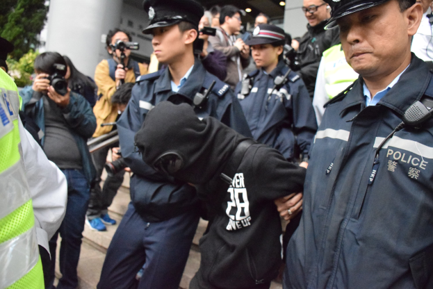 Eine Gruppe von Polizeibeamten, die vor einer Menschenmenge mit Säulen und Deckenbeleuchtung stehen, mit Bäumen links im Bild.