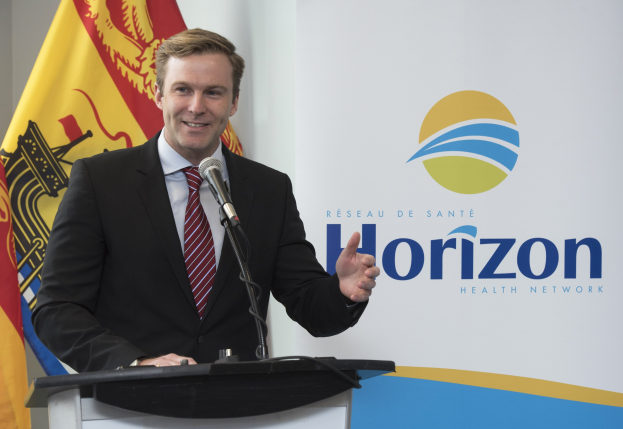 Ein Mann mit einem freundlichen Gesichtsausdruck in einem schwarzen Blazer, einem weißen Hemd und einer roten Krawatte steht an einem Podium mit einem Mikrofon, während er als CEO spricht, mit einem Banner im Hintergrund.
