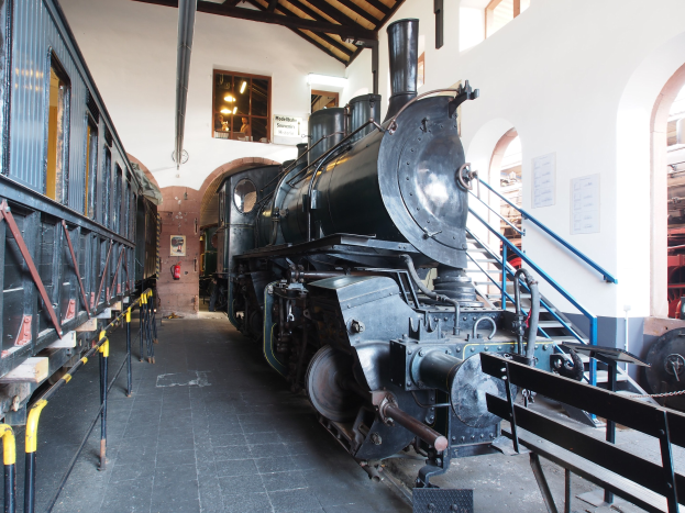 Alte Dampflokomotive in Museumsgebäude mit Informationsschildern und Geländern.