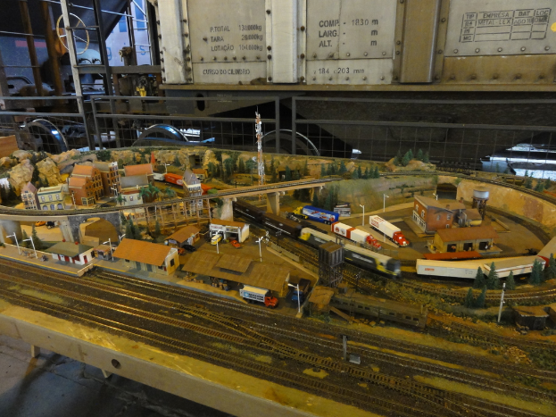 Eine Miniatur-Szene auf einem Tisch mit einer Eisenbahnschiene, einem Zug, Gebäuden, Fahrzeugen, einer Brücke, einem Turm und Bäumen.