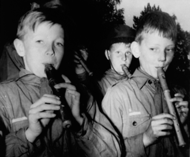 Gruppe junger Jungs, die Flöten im Freien spielen, mit Bäumen im Hintergrund.