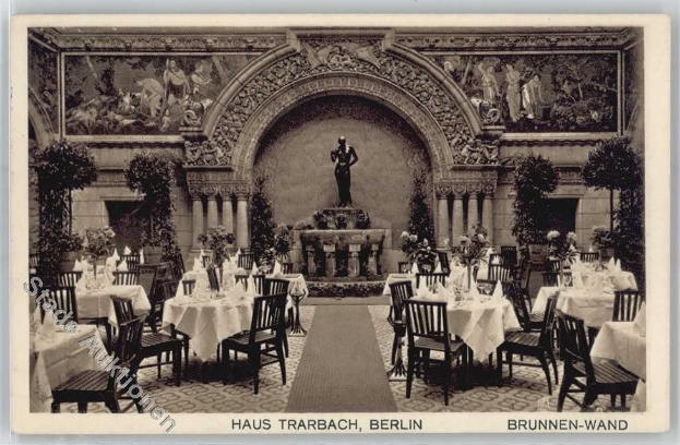 Ein altes Schwarz-Weiß-Foto eines Berliner Restaurants mit Tischen, Stühlen, Blumenvasen, einer Statue, Skulpturen, Pflanzen und Text unten.