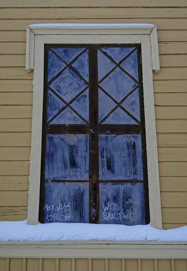 Ein altes Fenster an der Seite eines Hauses, das von einer leichten Schneeschicht bedeckt ist und von einer Wand eingerahmt wird.