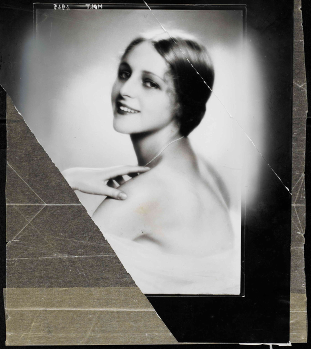 Schwarz-weißes Foto einer Frau in einem Kleid im Stil der 1920er Jahre mit einem ordentlichen Dutt, die direkt in die Kamera lächelt.