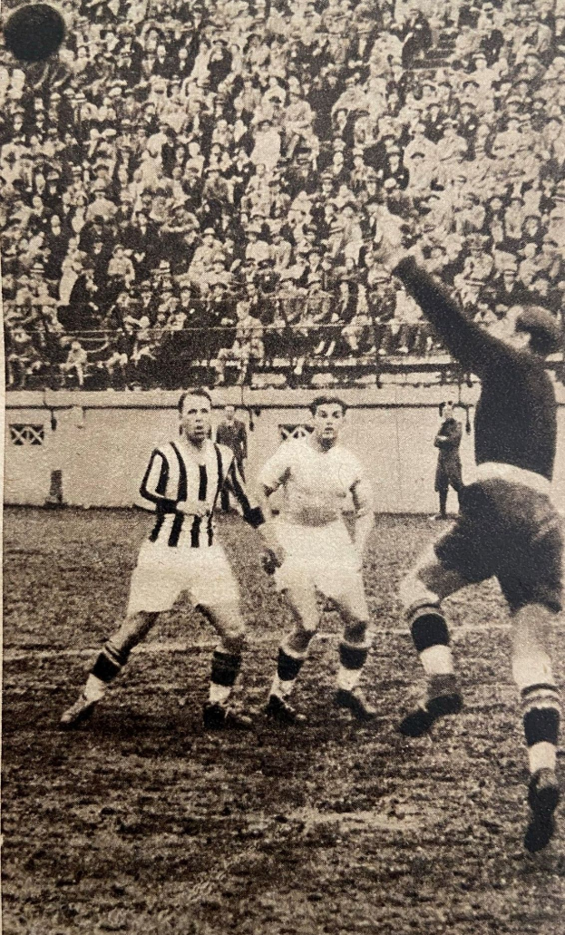 Ein Schwarz-Weiß-Foto einer Gruppe von Männern, die auf einem Feld Fußball spielen, mit einer Zuschauermenge im Hintergrund und einer Wand dahinter. Unten auf dem Bild steht der Text "Newcastle United v West Bromwich Albion".