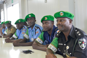 Gruppe von Polizeibeamten an einem Tisch während einer Schulung, mit Mobiltelefonen und anderen Gegenständen auf dem Tisch, in einem Raum mit Fenstern und Deckenbeleuchtung.