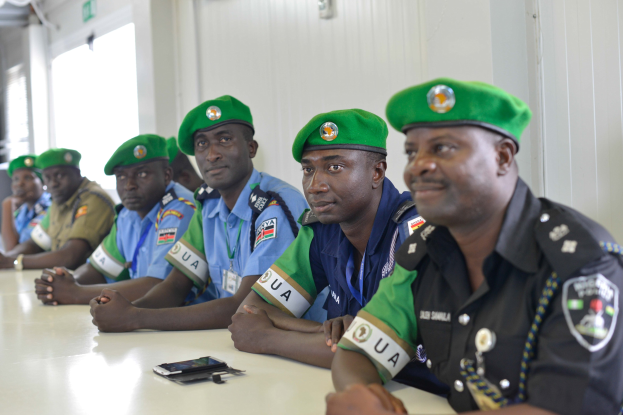 Gruppe von Polizeibeamten an einem Tisch während einer Schulung, mit Mobiltelefonen und anderen Gegenständen auf dem Tisch, in einem Raum mit Fenstern und Deckenbeleuchtung.