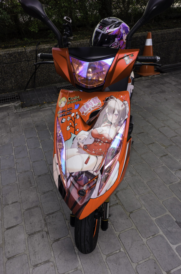 Oranger Roller mit Helm auf einer Straße geparkt, neben einer Verkehrsinsel, einer Wand und Bäumen.
