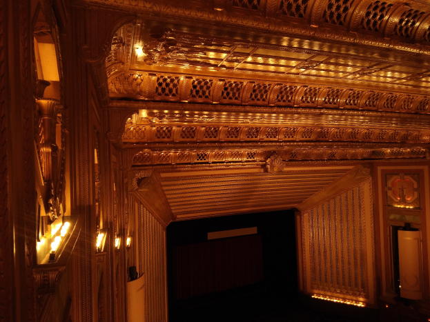 The interior of a theater with a dark background, illuminated by lights on the left and right, featuring an intricately designed ceiling.