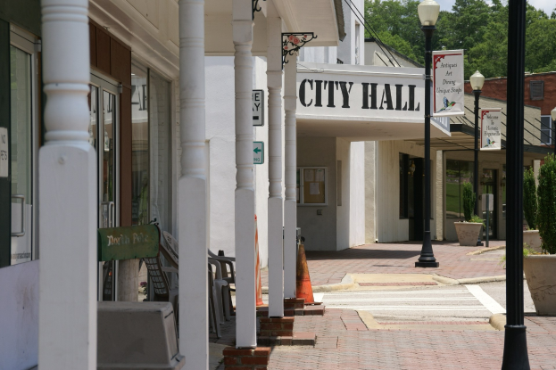 Stadthalle mit umliegenden Gebäuden, Straßeninfrastruktur, Fahrzeugen und Grünflächen unter einem bewölkten Himmel.