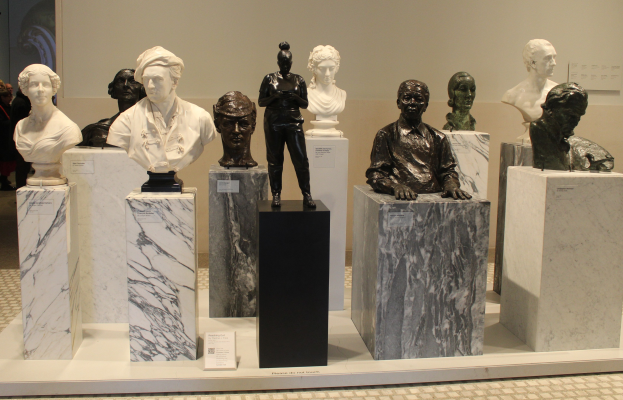 Gruppe detaillierter Büsten-Skulpturen in einem Museum ausgestellt, mit Besuchern im Hintergrund und einer Wand.