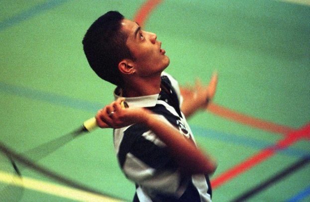 Ein junger Mann spielt Badminton auf einem Court, hält einen Schläger und hat einen entschlossenen Gesichtsausdruck.