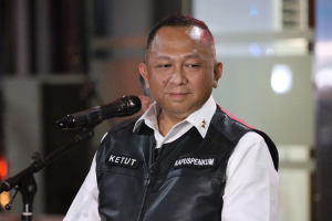 Ein Mann in einer schwarzen Weste und weißem Hemd steht vor einem Mikrofon und sieht besorgt aus, mit einem unscharfen Hintergrund.