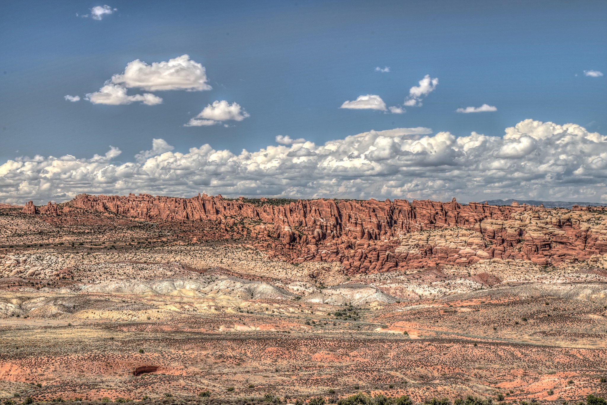 Wüstenlandschaft mit roten Felsen und spärlichen Bäumen unter einem bewölkten Himmel, mit einem Wasserzeichen unten.