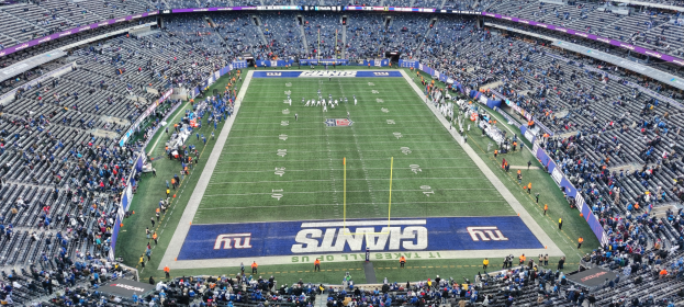 Ein voller Fußballstadion mit Spielern auf dem Feld, Zuschauern auf den Tribünen und Pfosten und Schildern rundherum.