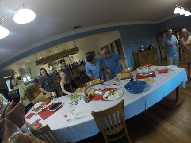 Eine Gruppe von Menschen steht in einem Haus um einen weißen Tisch in der Mitte mit Essen darauf.