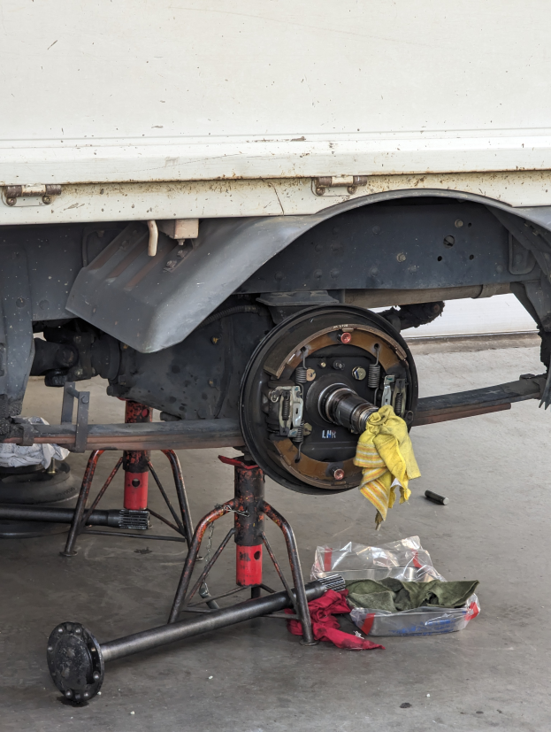Ein Lkw in einer Garage geparkt, mit einem gelben Tuch bedeckt, umgeben von verstreuten Werkzeugen und Gegenständen auf dem Boden.